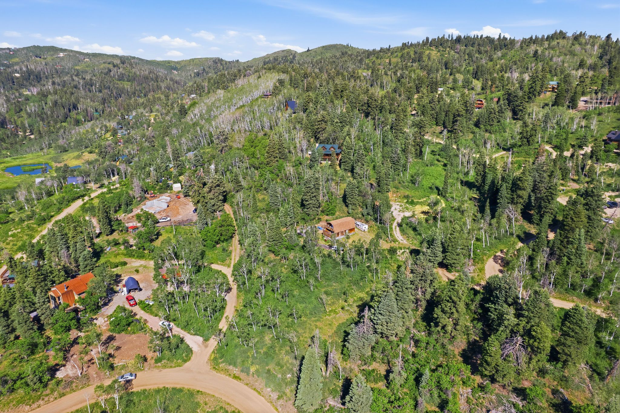 Expansive mountain property featuring varied terrain, a small pond, multiple structures, and extensive tree coverage