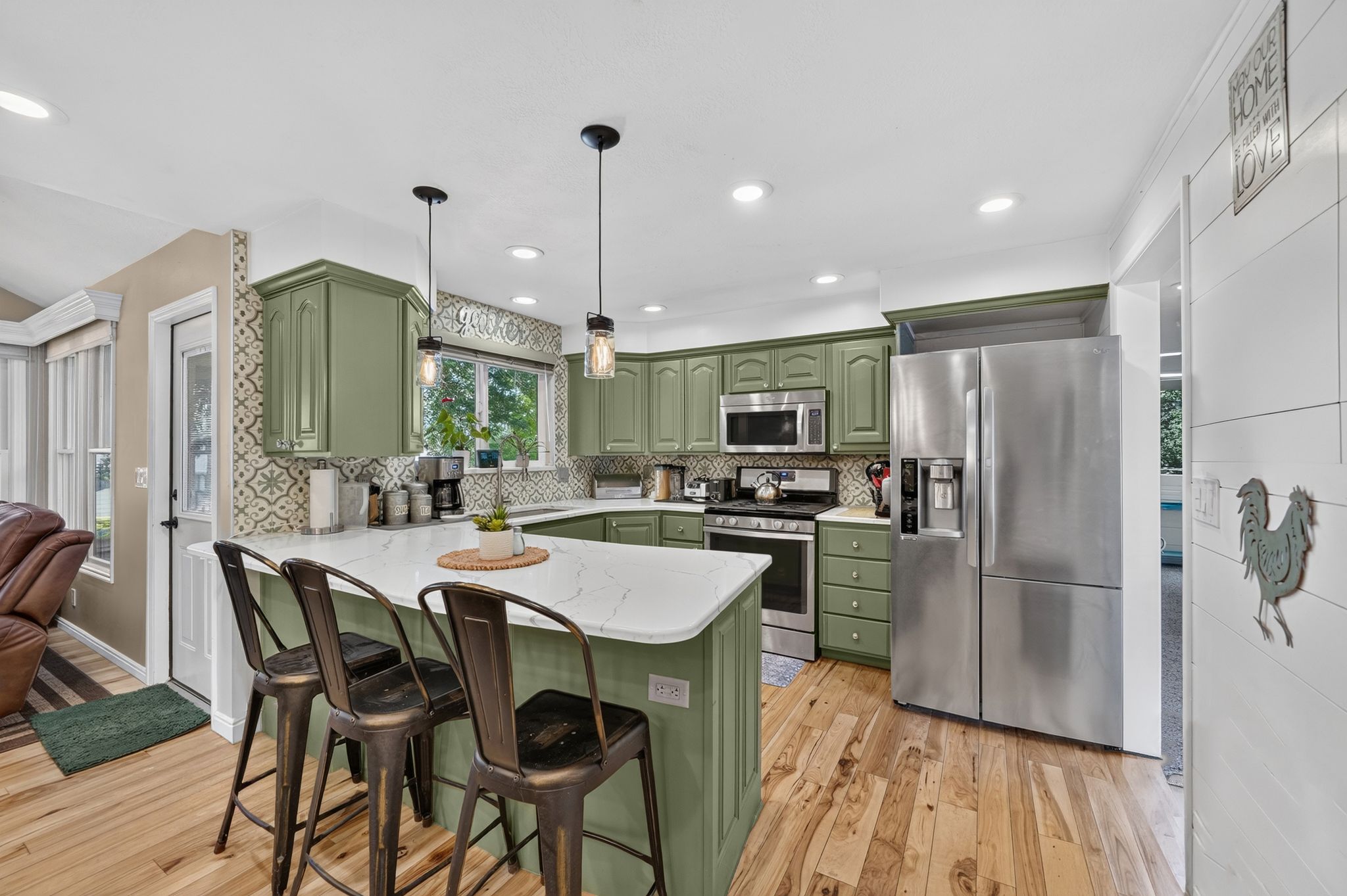 Kitchen featuring sage green cabinetry, stainless steel appliances, a white countertop island, pendant lighting, and wood-finish flooring