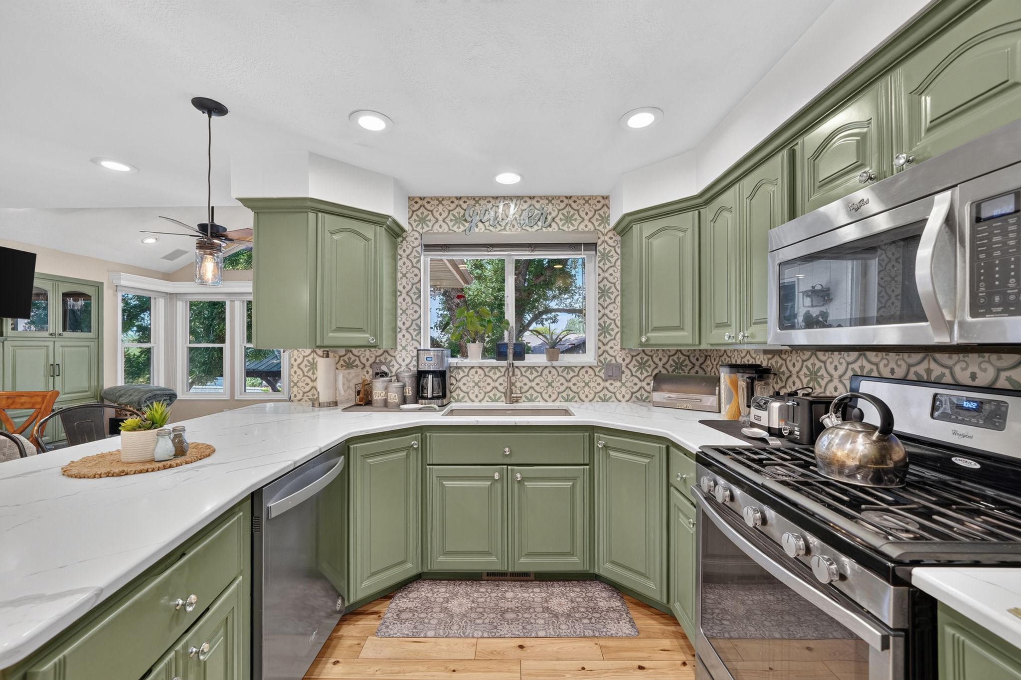 Kitchen featuring sage green cabinetry, stainless steel appliances, patterned tile backsplash, white countertops, and wood-finish flooring