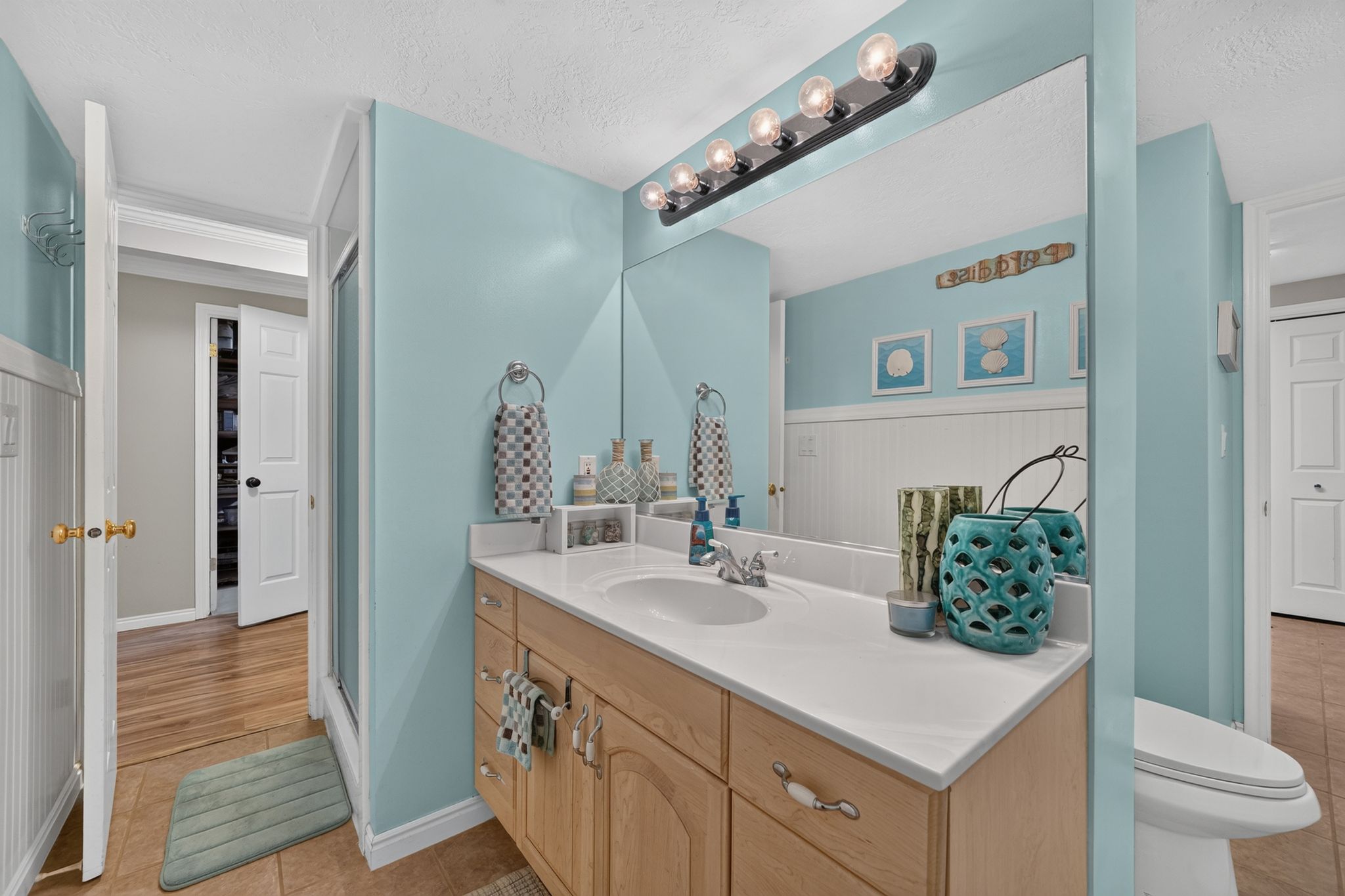 Bathroom vanity featuring a light wood-finish cabinet with white hardware, a white countertop, and an integrated sink