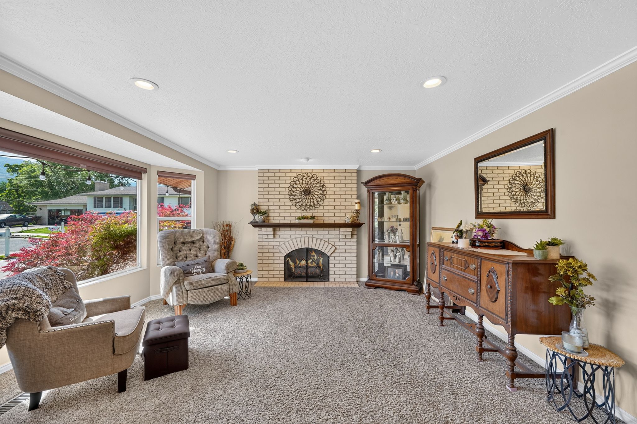 Spacious living area featuring a brick fireplace with a wood mantel, crown molding, recessed lighting, and a large bay window