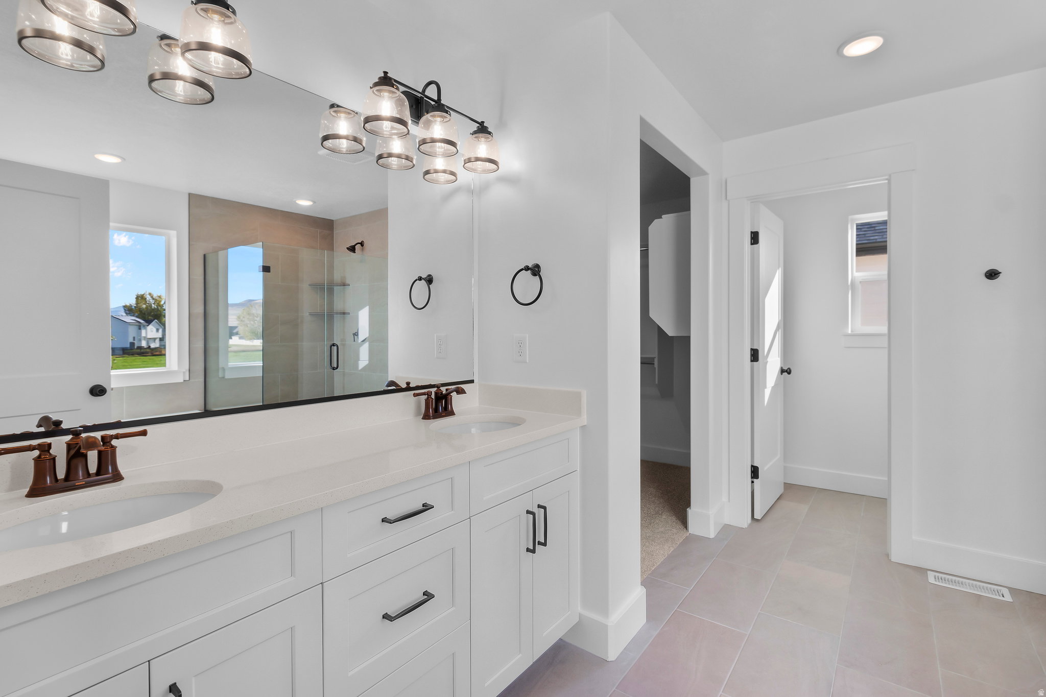 Bathroom featuring a double vanity with white cabinetry and integrated sinks, a wide mirror, and bronze-finish fixtures
