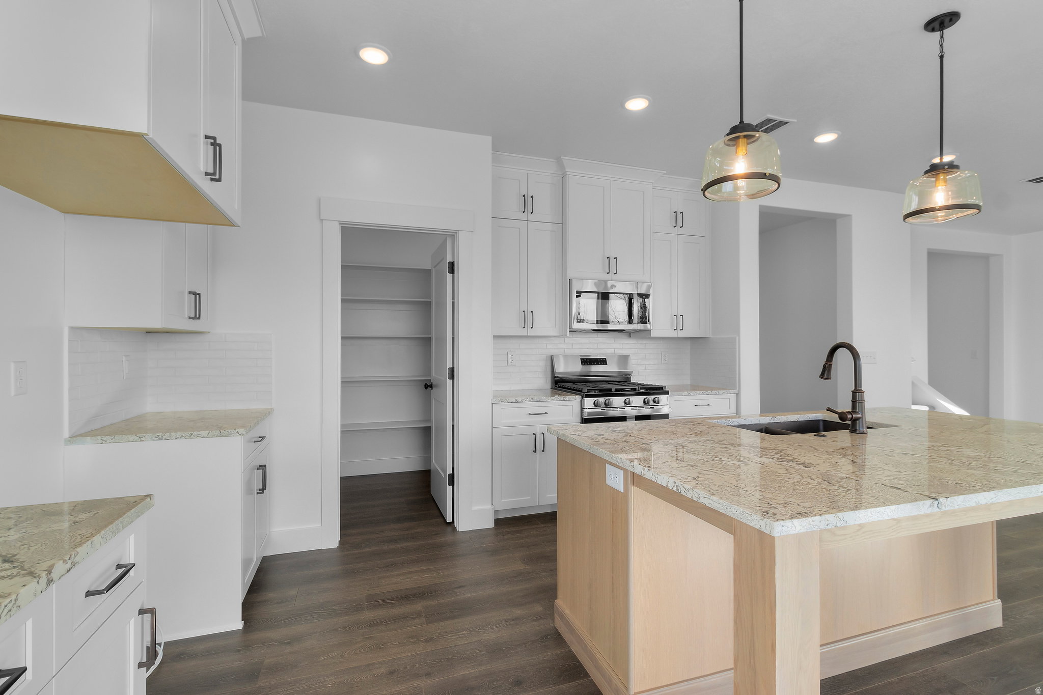 Kitchen featuring a central island with a light-toned countertop, white cabinetry with dark hardware, stainless steel appliances, a subway tile backsplash, and wood-finish flooring
