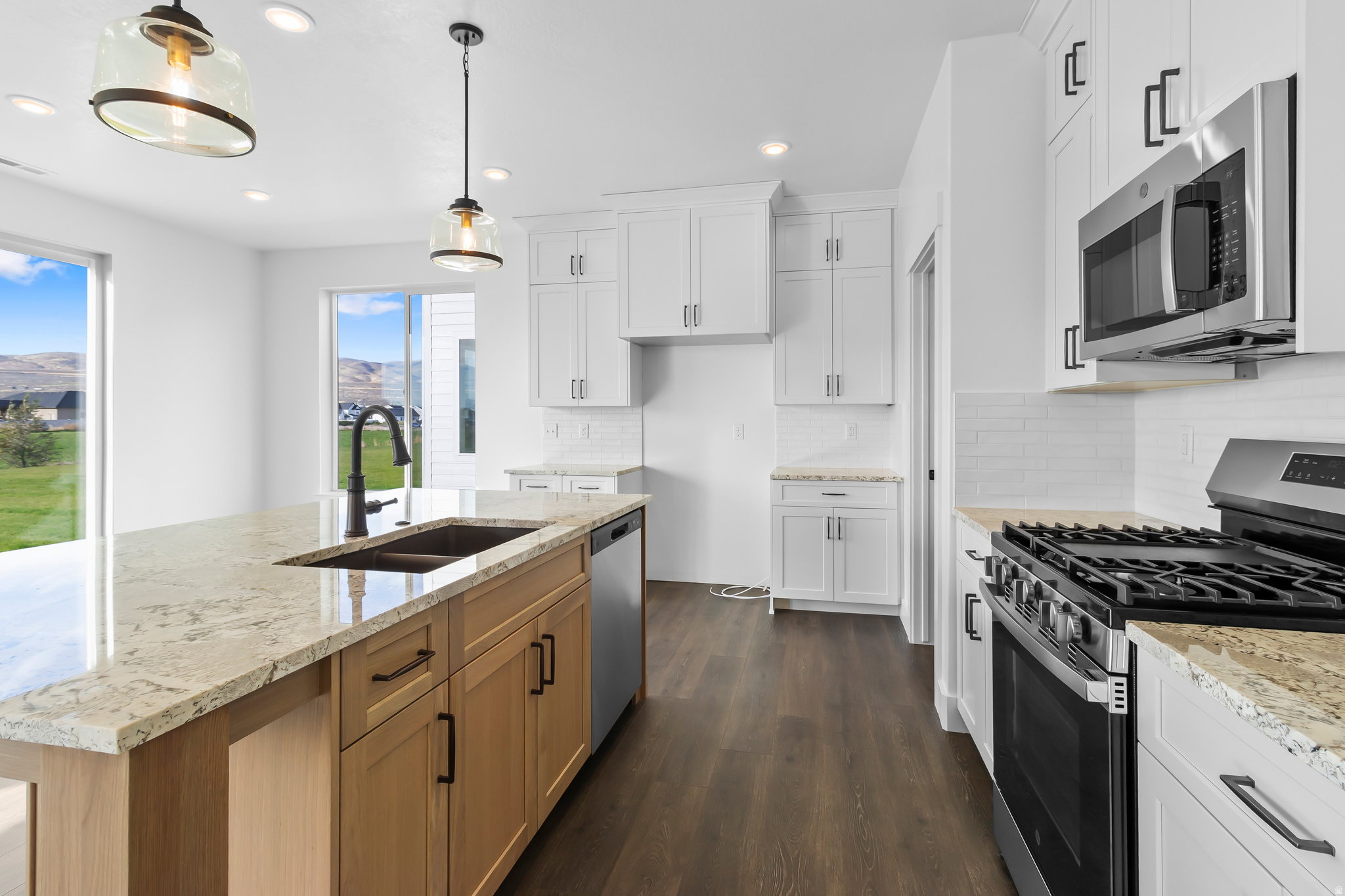 Kitchen featuring an island with a built-in sink and faucet, stainless steel appliances, white cabinetry, granite countertops, and dark wood-finish flooring
