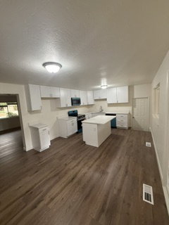 Open concept kitchen featuring an island, white cabinetry, dark contrasting appliances, and wood-finish flooring