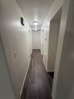 Hallway featuring dark wood-finish flooring, white baseboards, and neutral wall paint