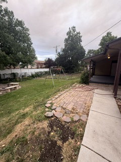 Spacious backyard featuring a concrete walkway, brick paver patio, a built-in stone fire pit area, and mature trees