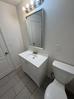Bathroom featuring a white vanity with integrated sink, rectangular mirror, and overhead four-bulb light fixture