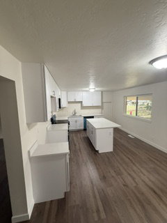 Open-concept kitchen featuring wood-finish flooring, white cabinetry, light countertops, a central island, and recessed lighting