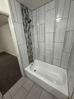 Bathtub with a shower featuring a tiled surround and mosaic accent strip