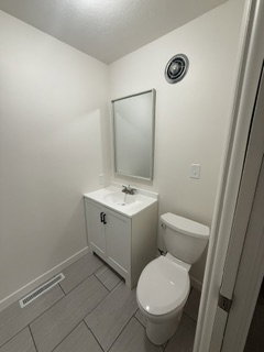 Powder room featuring a white single-sink vanity with a white countertop, chrome faucet, rectangular wall mirror, and modern gray tile flooring