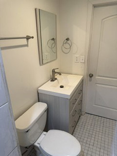 Bathroom featuring a contemporary vanity with an integrated sink and brushed nickel faucet, a wall-mounted rectangular mirror, and a white toilet