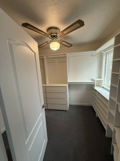 Walk-in closet featuring extensive built-in shelving, integrated drawer storage, and a ceiling fan with integrated lighting