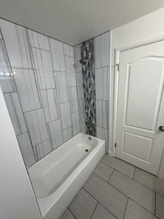 Bathtub with floor-to-ceiling tile surround, featuring a decorative vertical accent mosaic