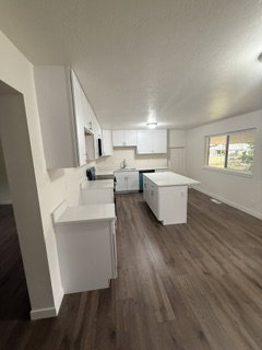 Modern kitchen featuring white cabinetry, light countertops, a central island, wood-finish flooring, and a large window