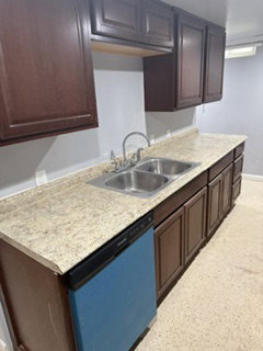 Kitchen featuring dark wood-finish cabinetry, light speckled countertops, and a double basin stainless steel sink with a gooseneck faucet