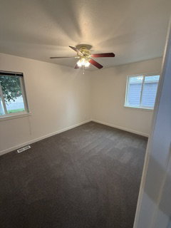 Room featuring neutral-toned walls, dark patterned carpeting, and a ceiling fan with integrated lighting