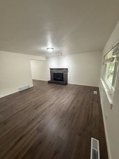 Living room featuring wood-finish flooring, a stone-faced fireplace, white walls, and an overhead light fixture