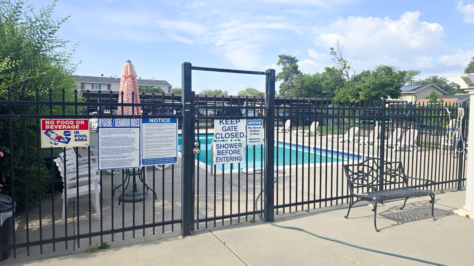 Secured outdoor swimming pool area featuring a perimeter fence, concrete decking, and sun loungers