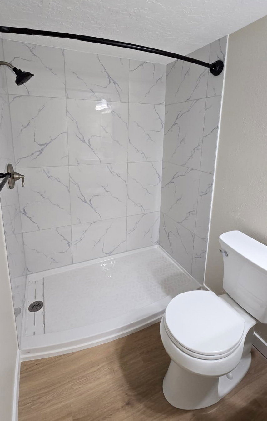 White tile shower surround with grey veining, brushed nickel shower fixtures, and a curved black shower rod