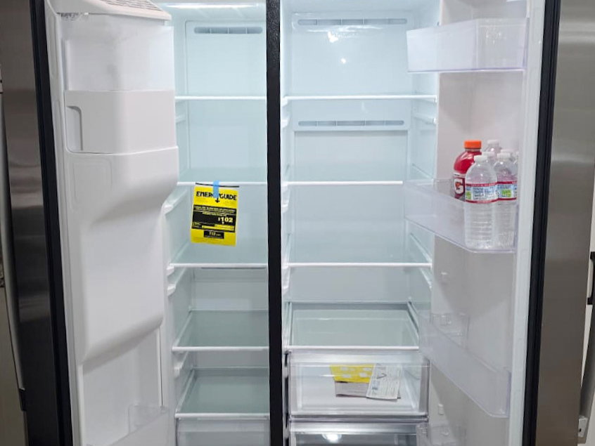 Stainless steel side-by-side refrigerator featuring interior lighting, multiple adjustable glass shelves, clear door bins, and bottom crisper drawers