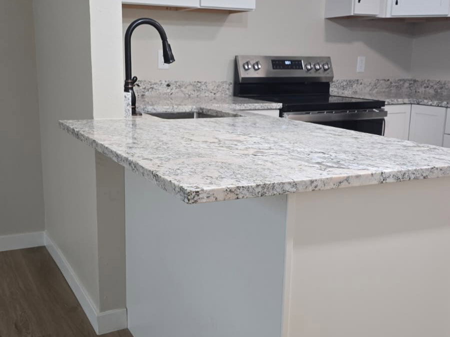 Kitchen island with light-toned granite countertop, featuring a black gooseneck faucet and undermount sink