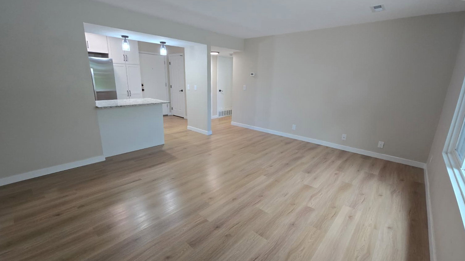 Spacious open-concept living area featuring wood-finish flooring, neutral wall tones, and white baseboards