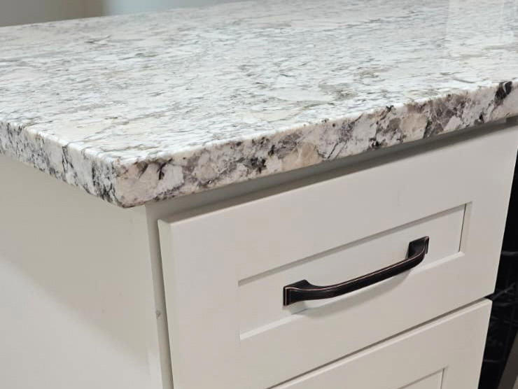 White shaker-style cabinetry featuring black hardware, a light-toned countertop, and wood-finish flooring