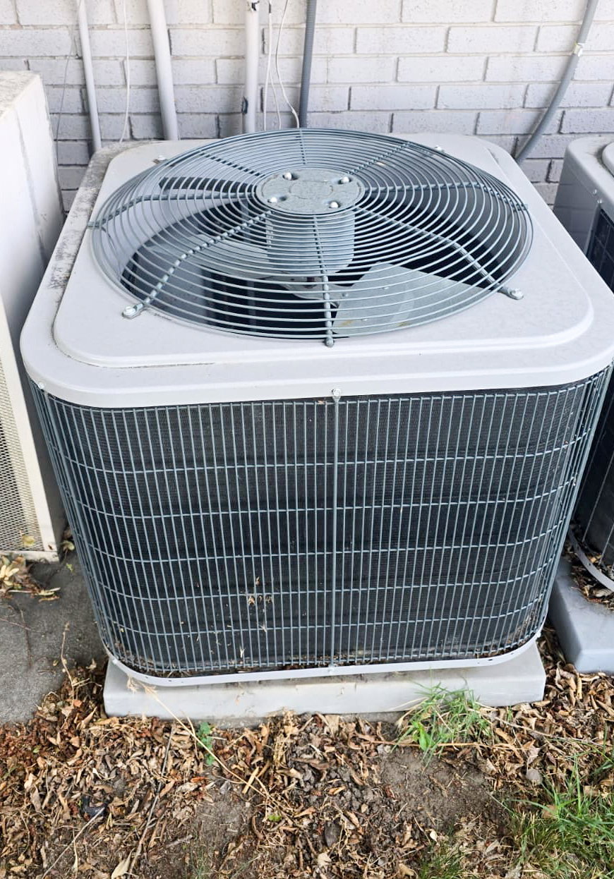 Outdoor HVAC unit featuring a top-mounted fan, protective grille, and a concrete pad foundation