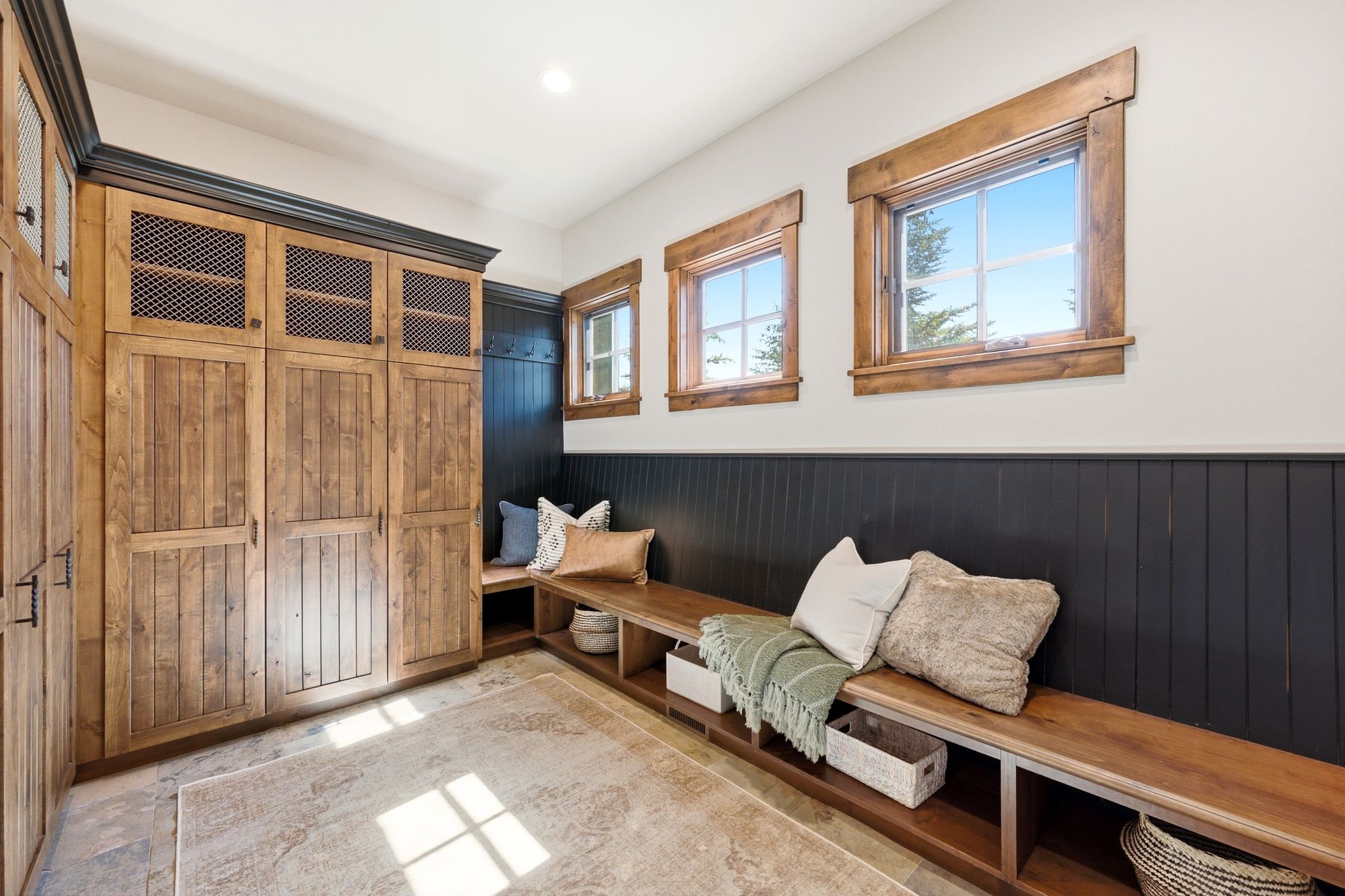 Built-in wood cabinetry with metal mesh accents, integrated bench seating with open storage, dark wood wainscoting, and natural wood window trim