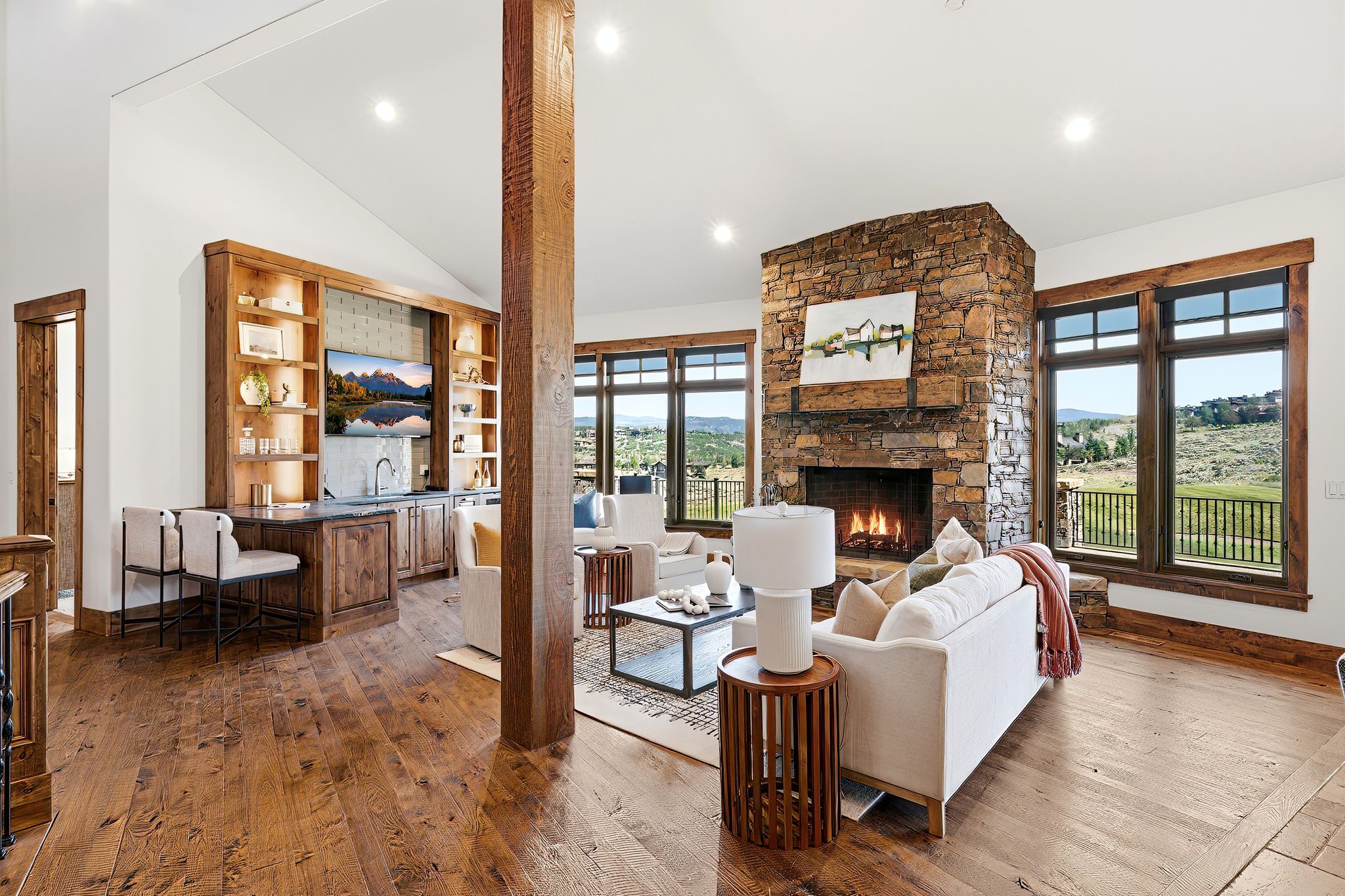 Spacious living area featuring a stone fireplace, wood-finish flooring, and a built-in wet bar with shelving