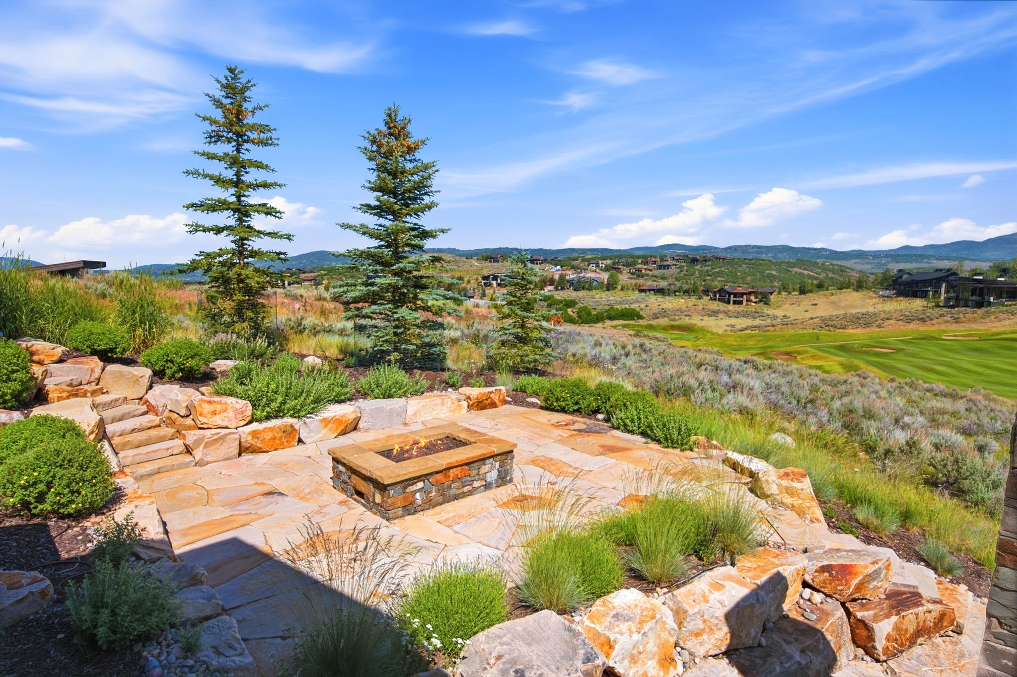 Expansive stone patio featuring a built-in fire pit, multiple levels, and natural rock landscaping