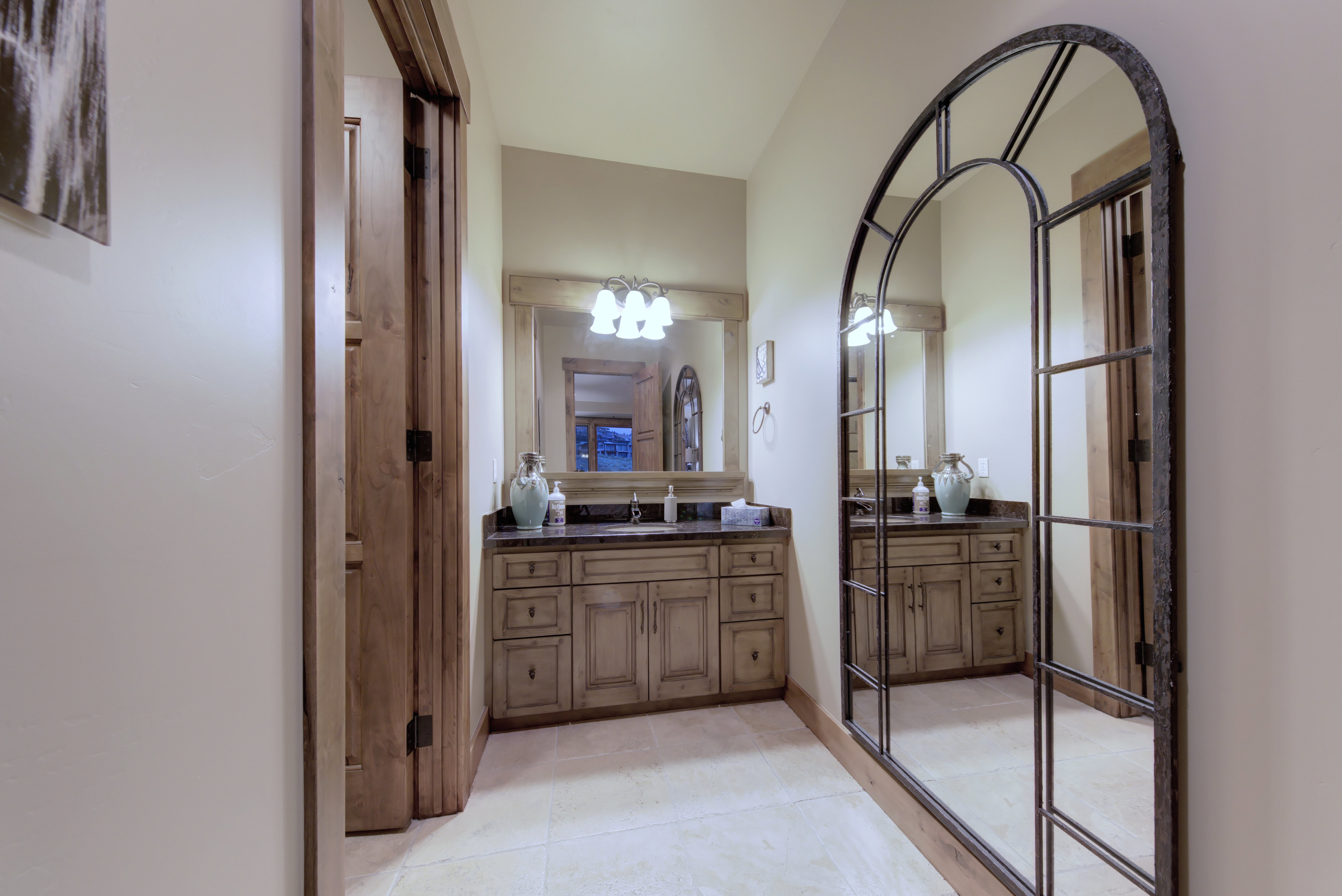 Vanity area featuring a dual sink wood vanity with a dark countertop and a decorative arched mirror