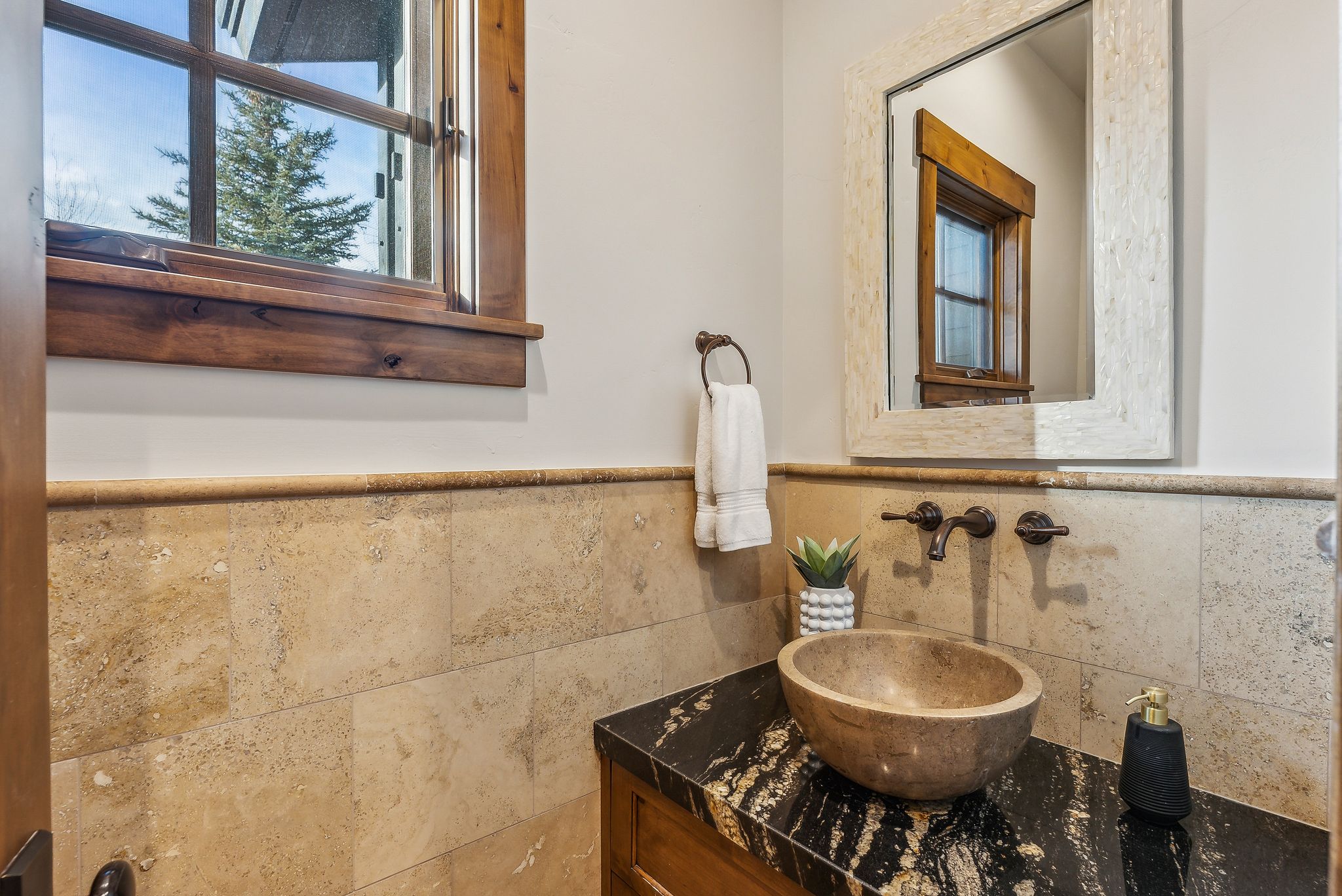 Vanity featuring a stone vessel sink, dark stone countertop, and wall-mounted faucet