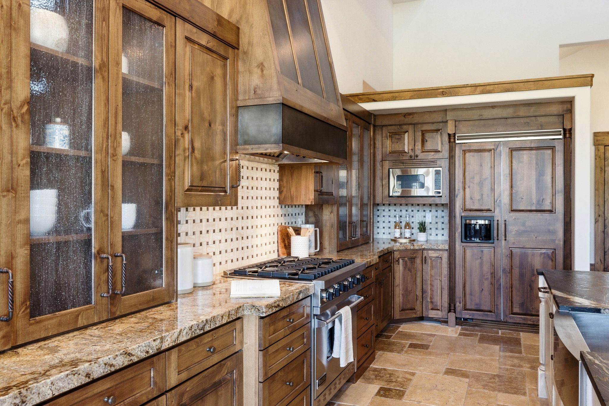 Gourmet kitchen showcasing custom wood cabinetry with glass-front uppers, granite countertops, a professional-grade gas range, and integrated panel-ready appliances