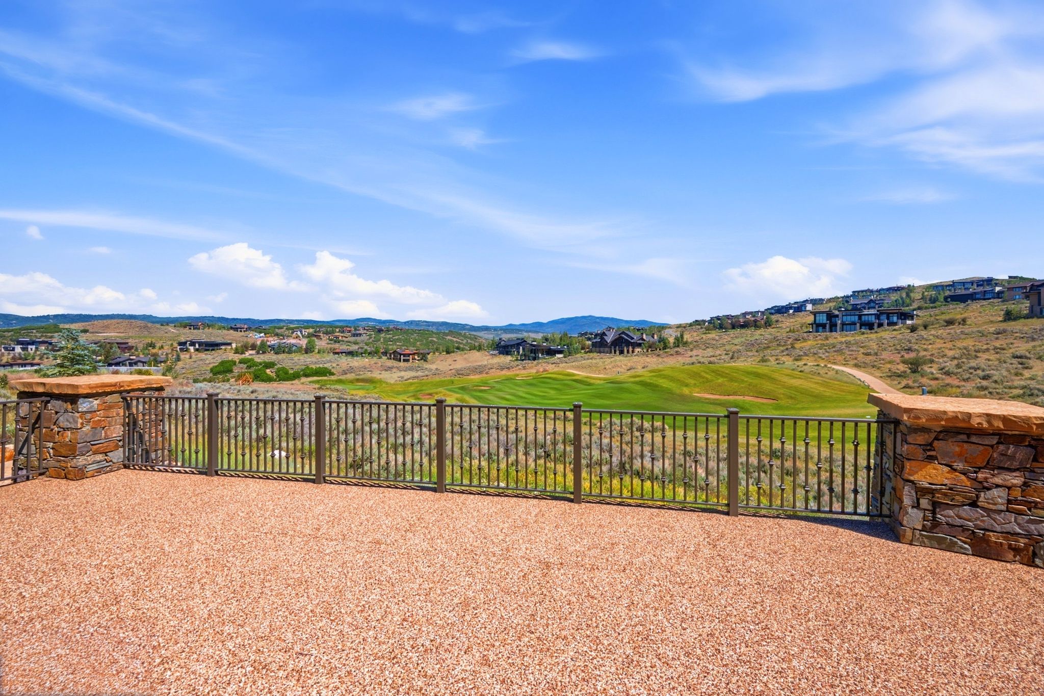 Spacious outdoor patio with a textured aggregate surface, stone pillars, and metal railings