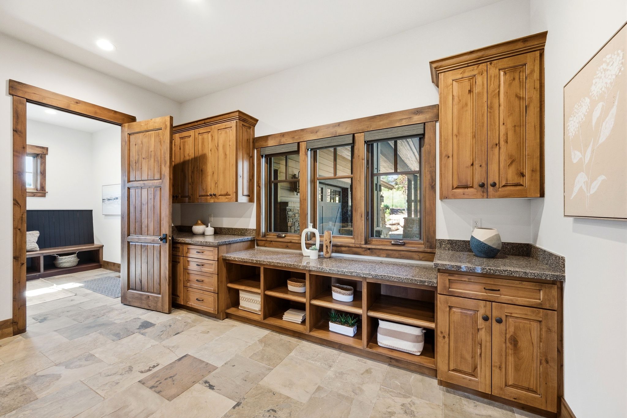 Light-toned stone tile flooring, natural wood cabinetry with stone countertops, and built-in shelving