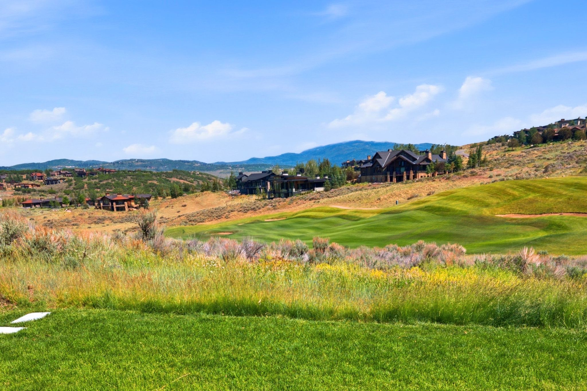 Expansive golf course property with distant mountain range, featuring a sloped, manicured green and scattered native grasses