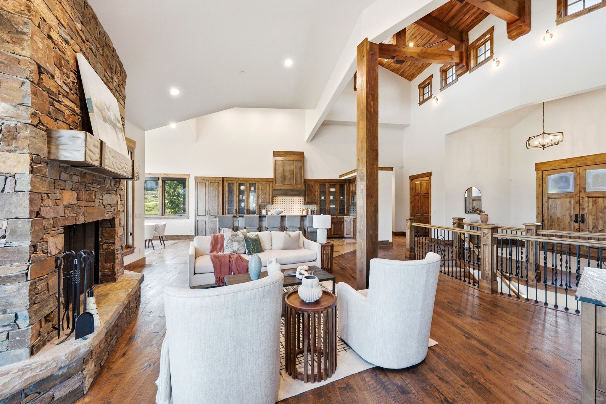 Great room featuring a prominent stone fireplace, vaulted ceilings with exposed wood beams, and hardwood flooring