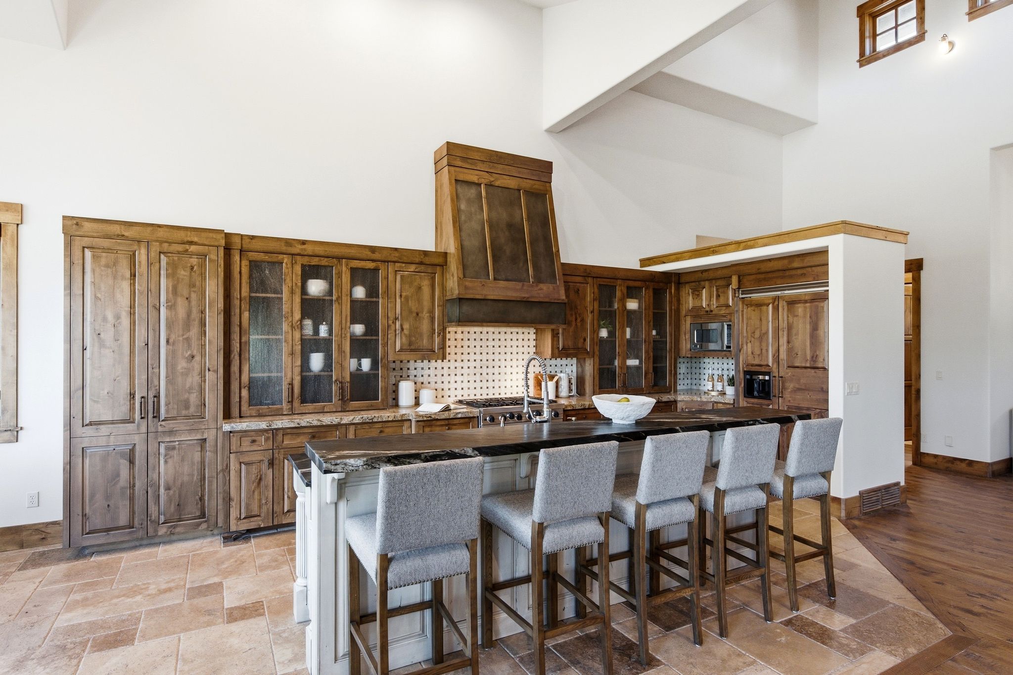 Gourmet kitchen featuring custom wood cabinetry, a large center island with seating, dark countertops, a decorative range hood, and tile flooring