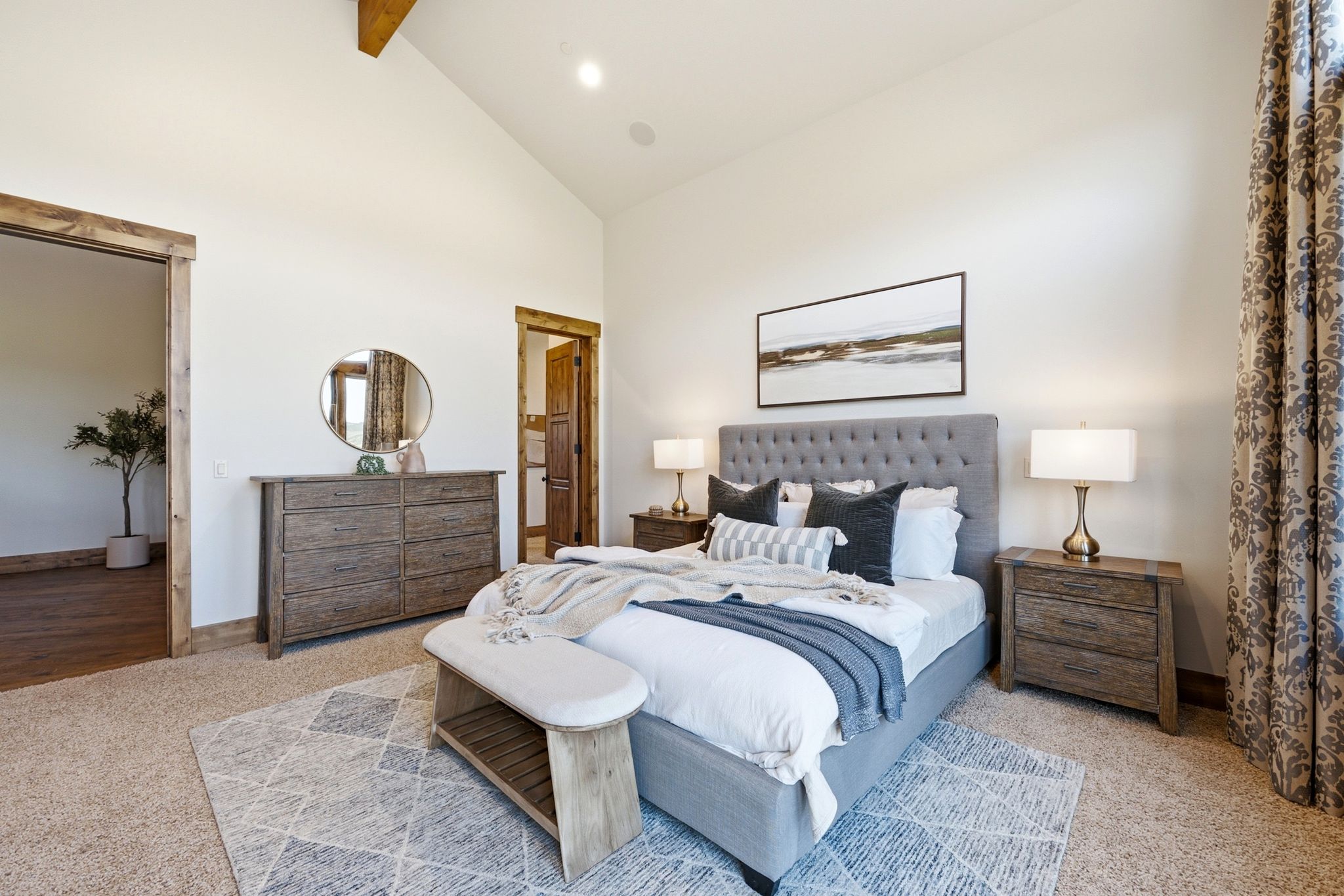 Spacious bedroom featuring a vaulted ceiling with exposed wood beam, light-colored carpet flooring, and a doorway with wood trim