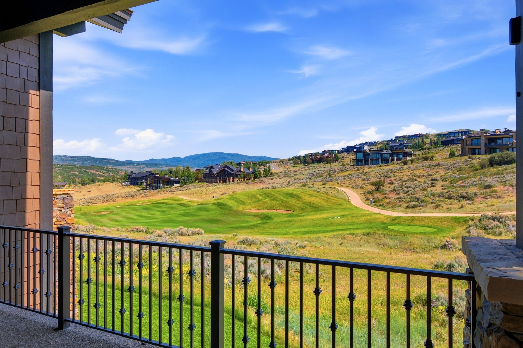 Balcony with wrought iron railing and stone column, overlooking a golf course with green fairways and distant mountainous terrain