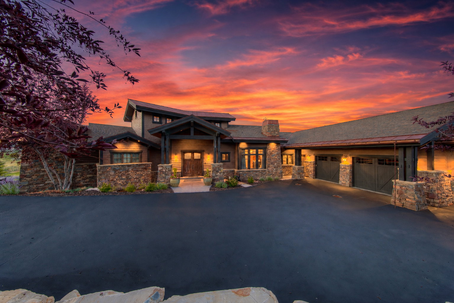 Craftsman-style facade featuring stone accents, a deep covered entry, wood siding, and multiple attached garage bays