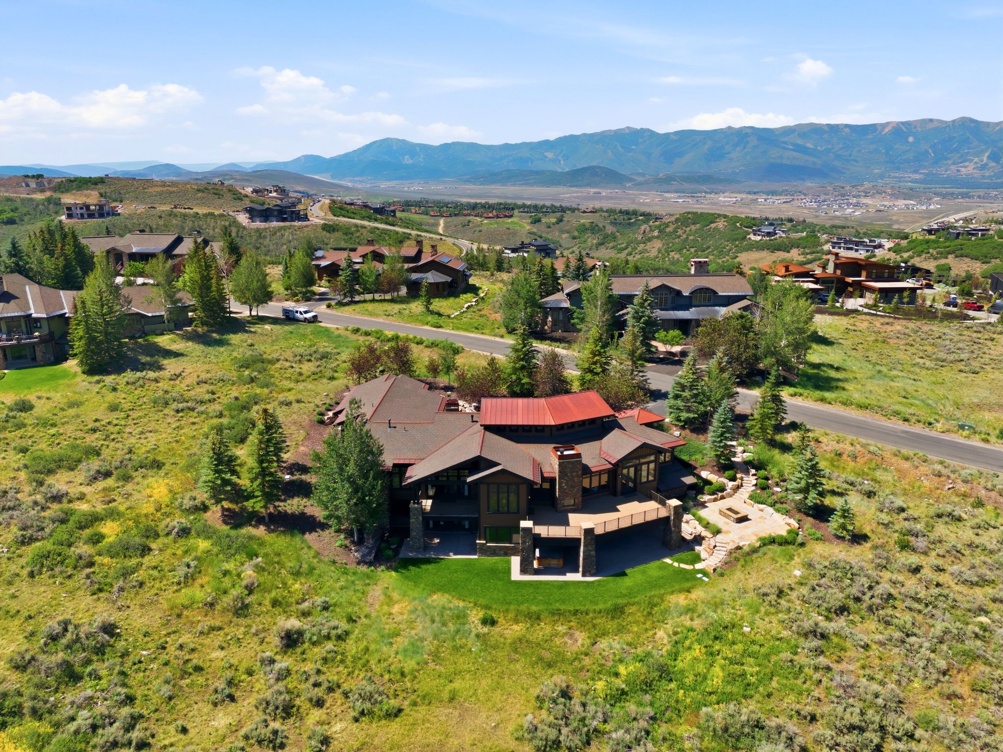 Hillside property featuring a multi-level design with a red metal roof, extensive outdoor decking, and a built-in fire pit