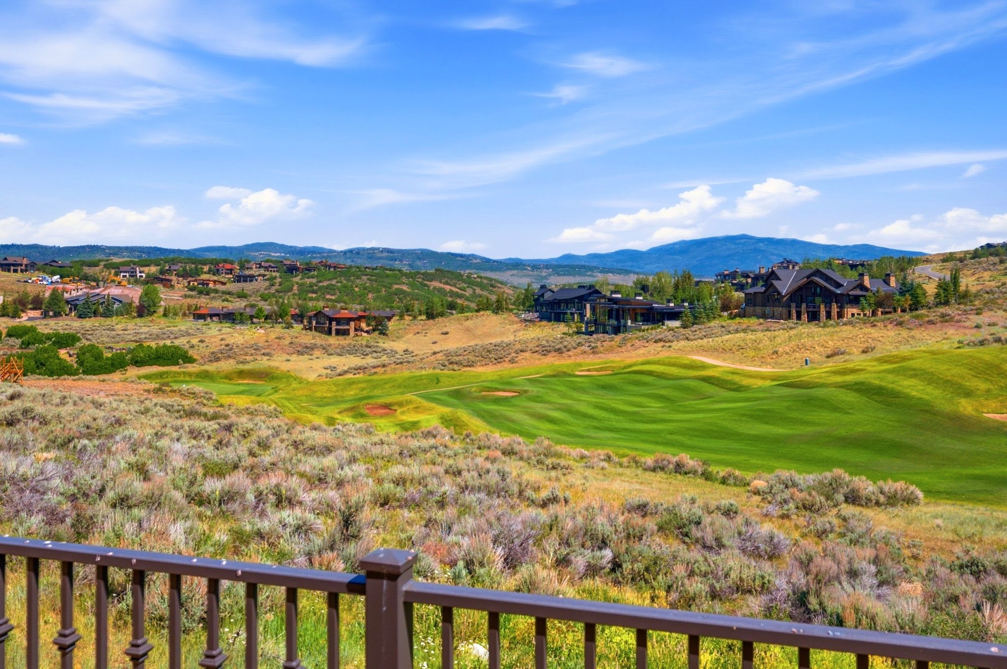 Expansive mountain landscape featuring a lush golf course, scattered residential properties, and distant mountain ranges