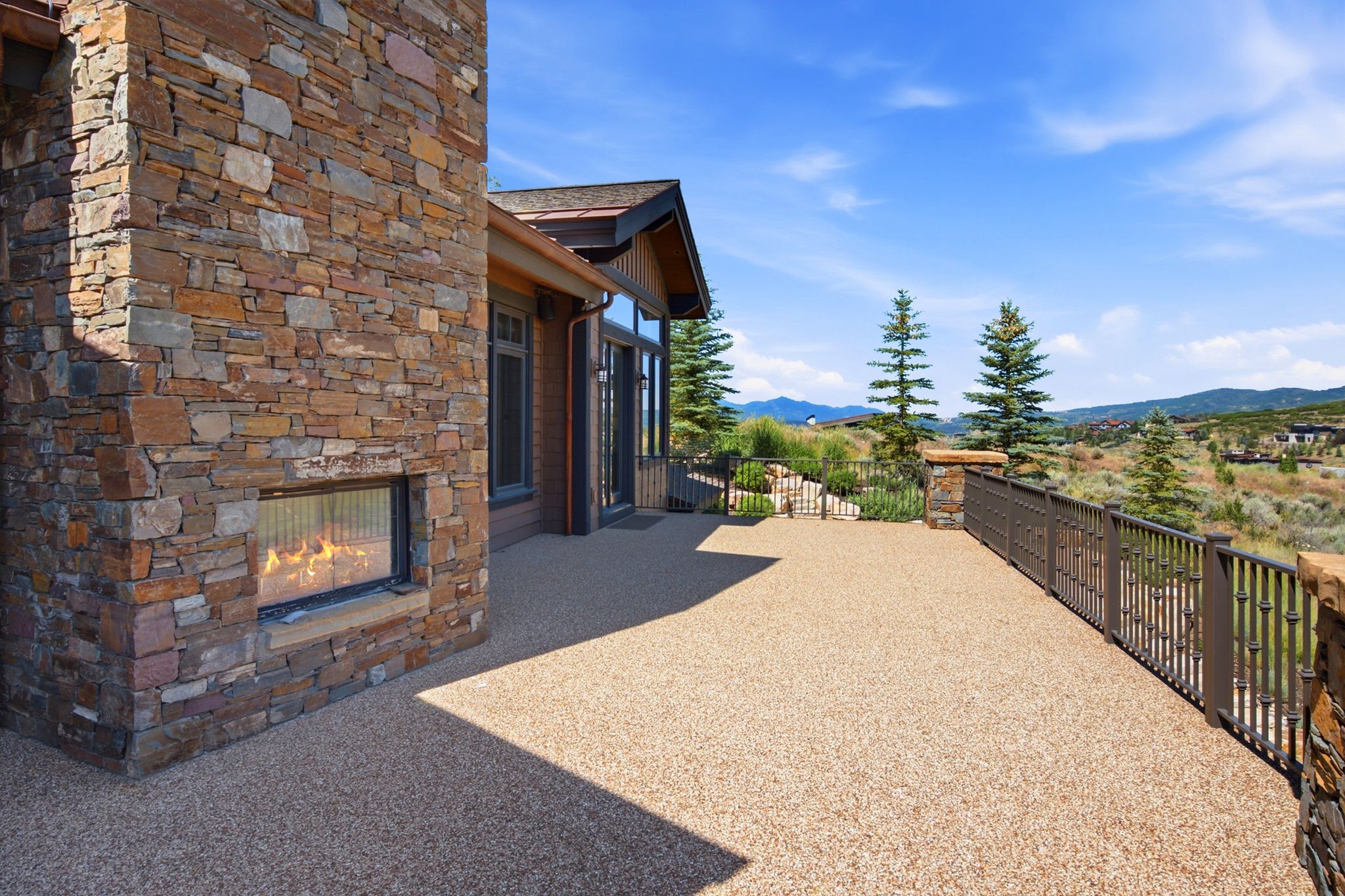 Expansive outdoor patio featuring an exterior stone fireplace, decorative metal railing, and a durable aggregate surface