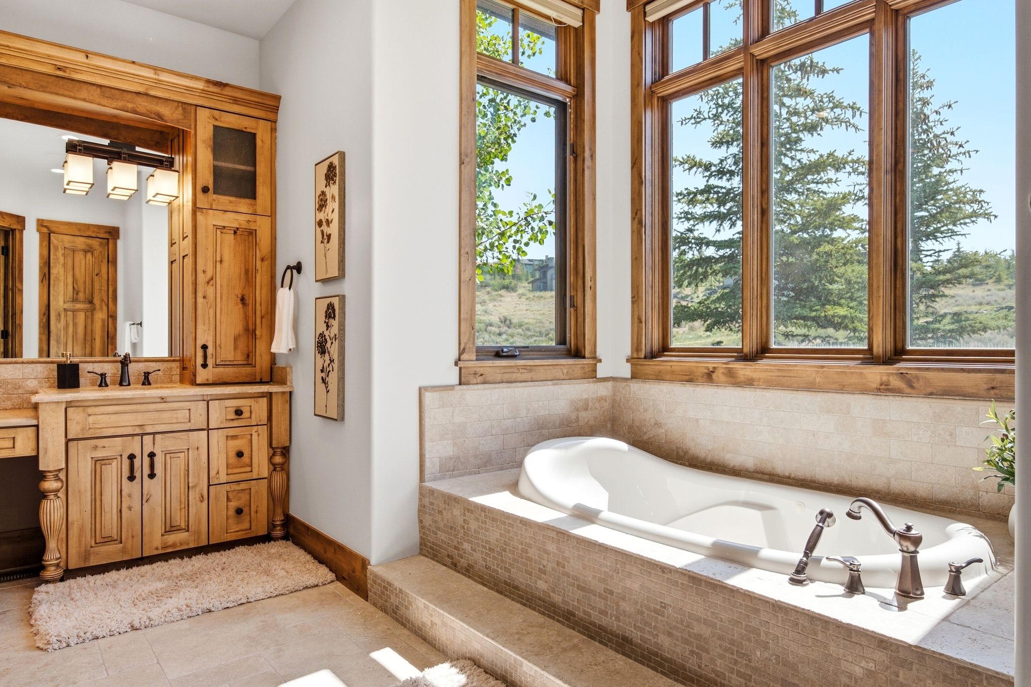 Soaking tub set within a tiled surround, featuring bronze fixtures and expansive wood-framed windows