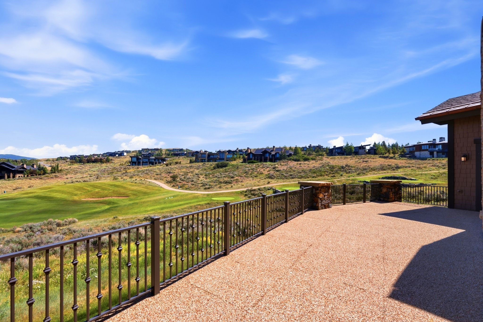 Spacious outdoor patio with an exposed aggregate finish, featuring wrought iron railings and stone pillars