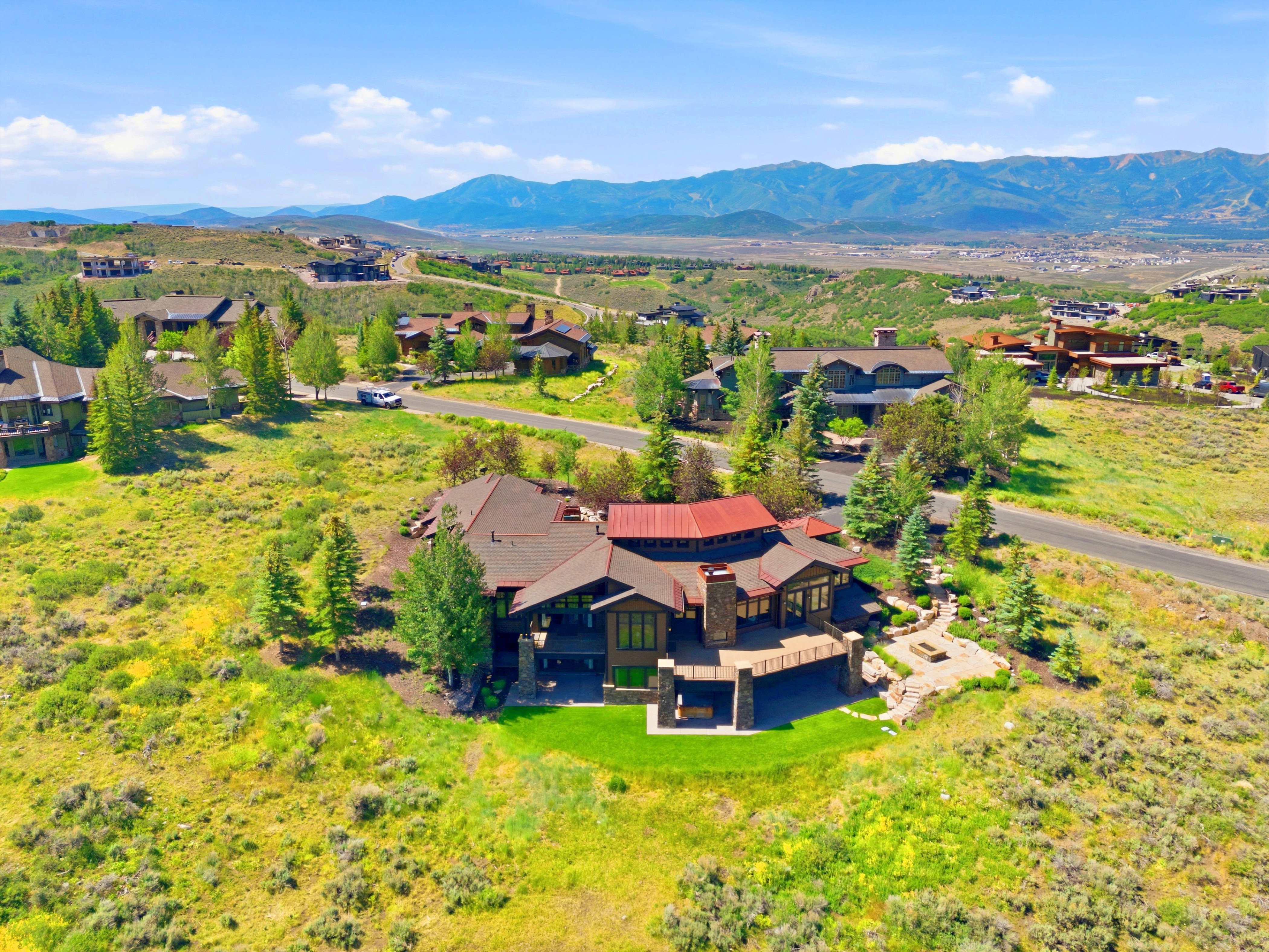 Expansive property featuring a multi-level residence with a red metal roof, stone accents, and a large outdoor deck