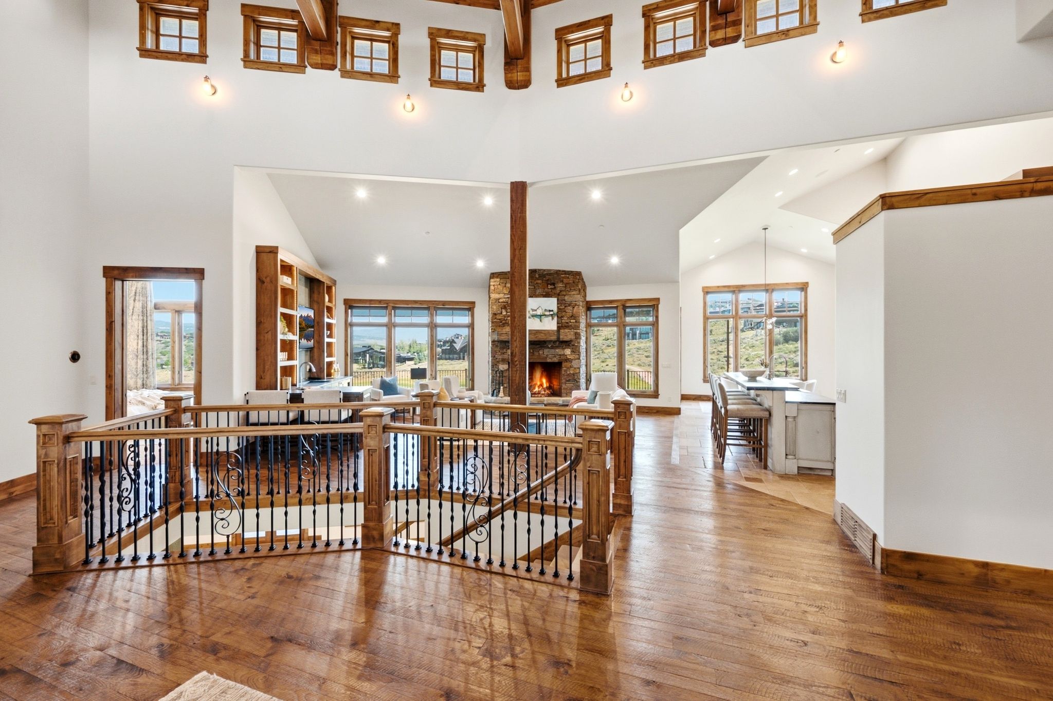Two-story foyer featuring wood-finish flooring, a wood and iron railing, vaulted ceilings with exposed wood beams, and a stone fireplace